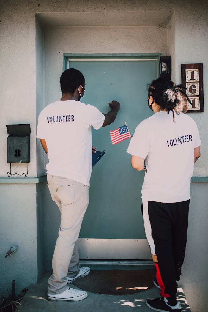 Two volunteers knocking on a residential door holding an American flag, promoting community engagement.